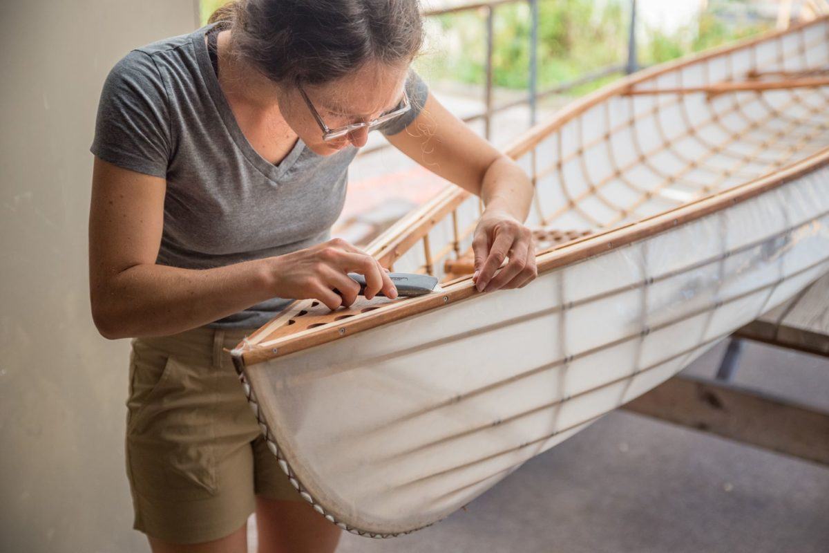 A young woman using a tool as she works on a canoe