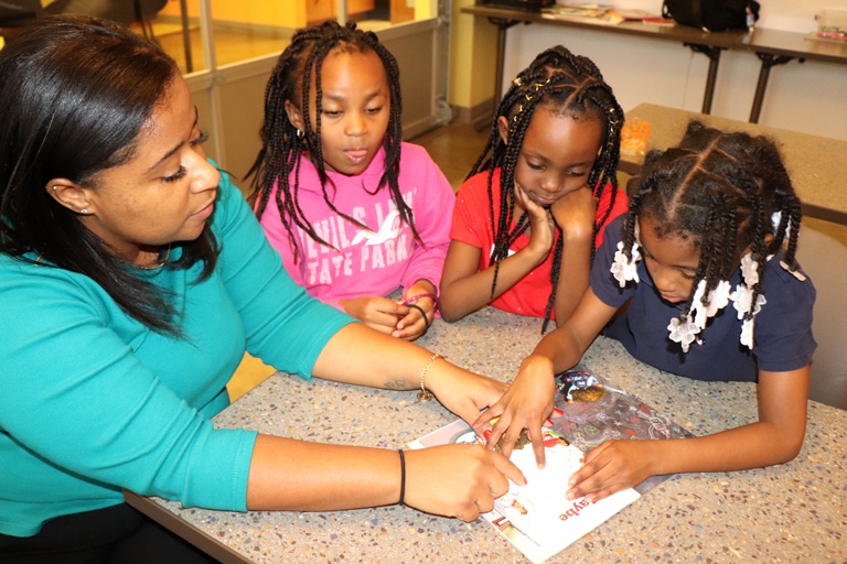 Three young girls reading a book at a table with a mentor