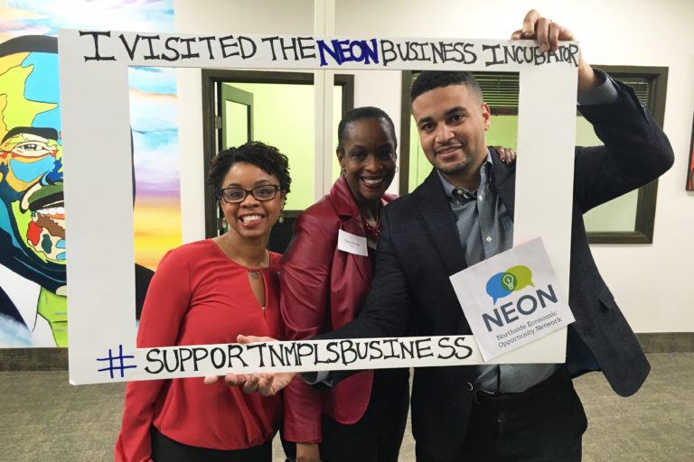 Three people holding sign for NEON's incubator fundraising campaign.